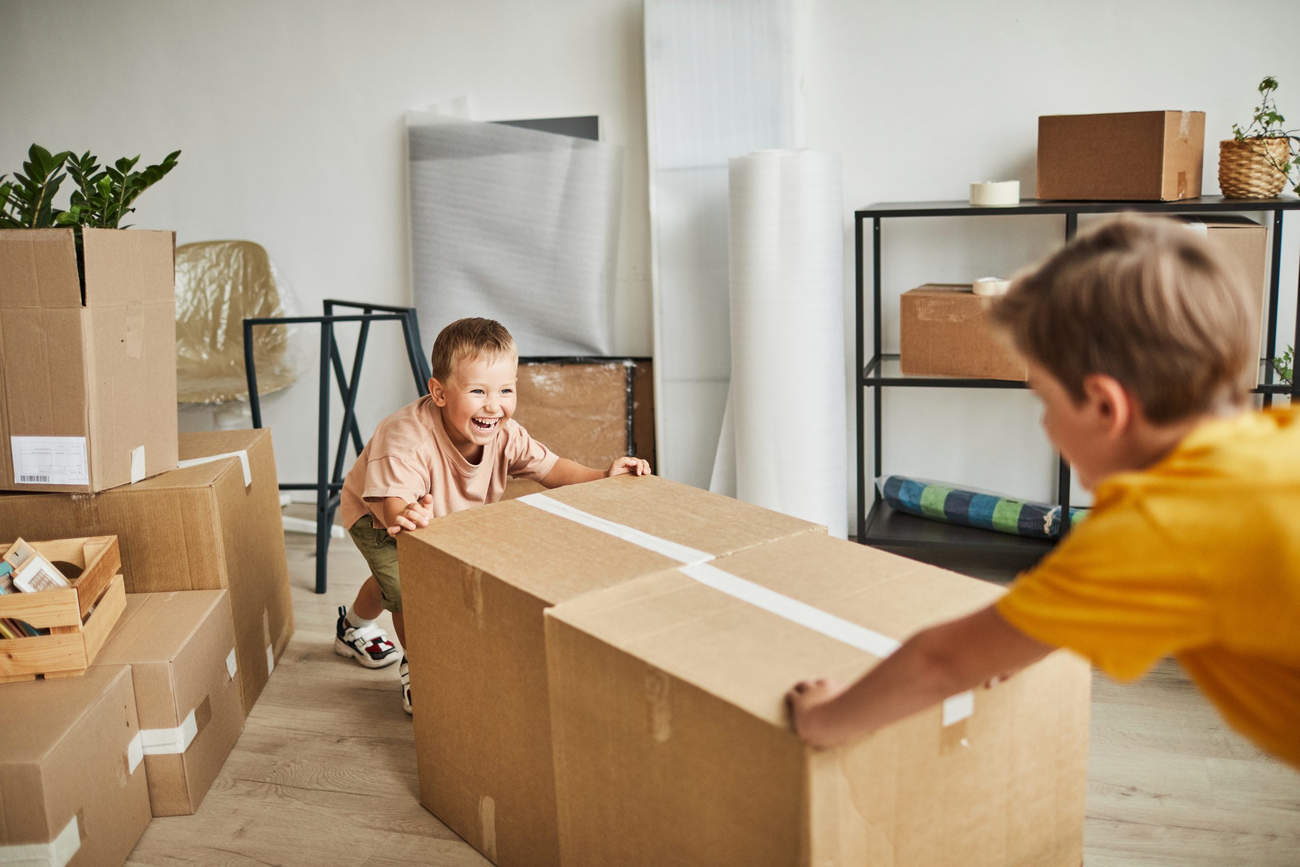 Portrait of two happy boys moving boxes and playing while family relocating to new house, copy space