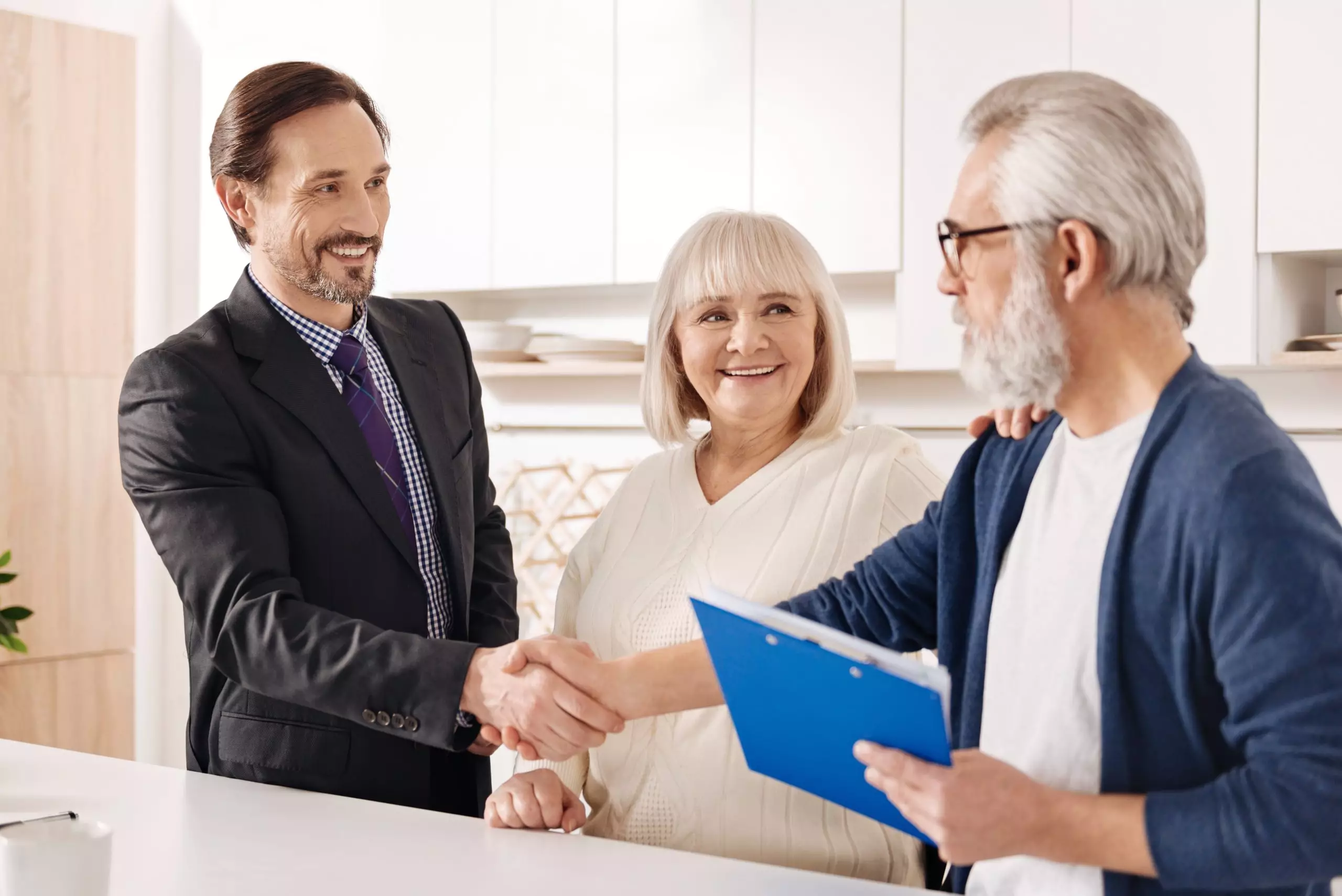 Meeting future owners of the house. Delighted experienced positive real estate agent meeting with old couple of clients while shaking hands and presenting contract