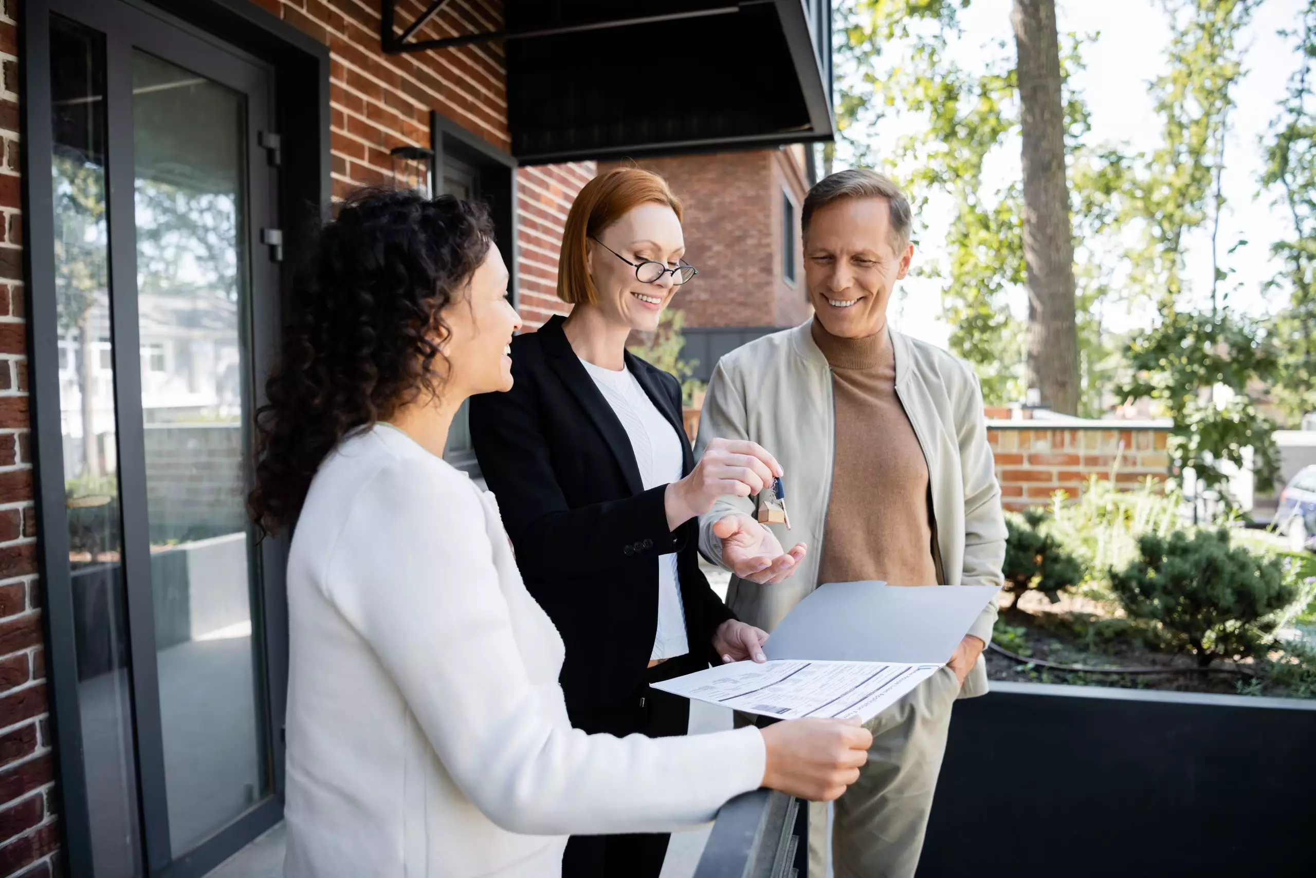 Happy realtor giving key to cheerful man near african american wife